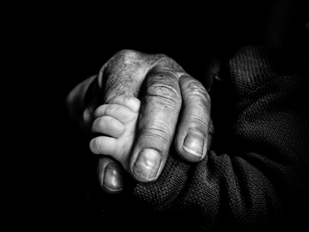 Opa hält behütend die Hand eines Säuglings